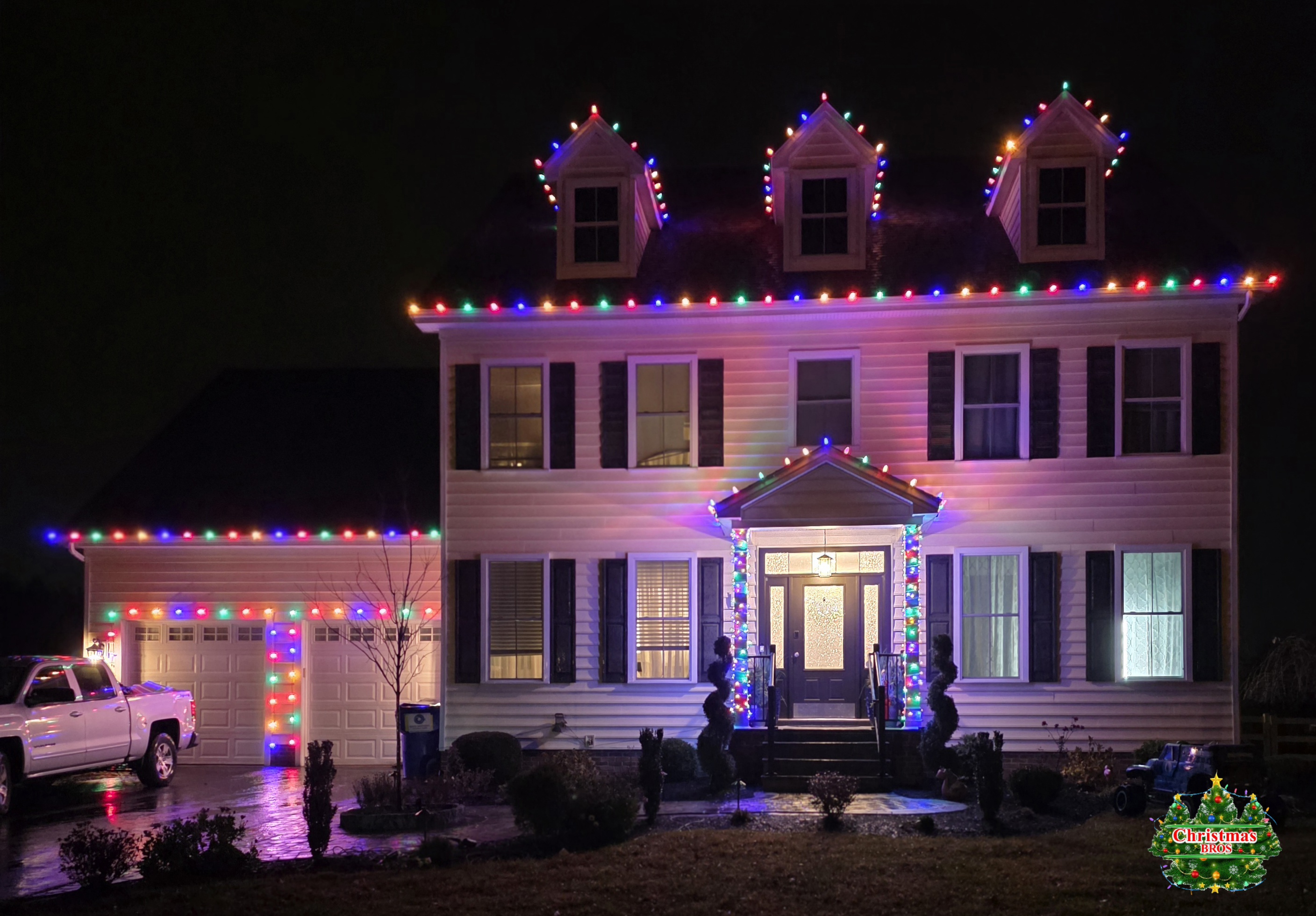 Full multicolor C9s — roofline, all three dormers, the garage wing, and the columns wrapped down both sides of the door. When a family wants color, we don't do it halfway.