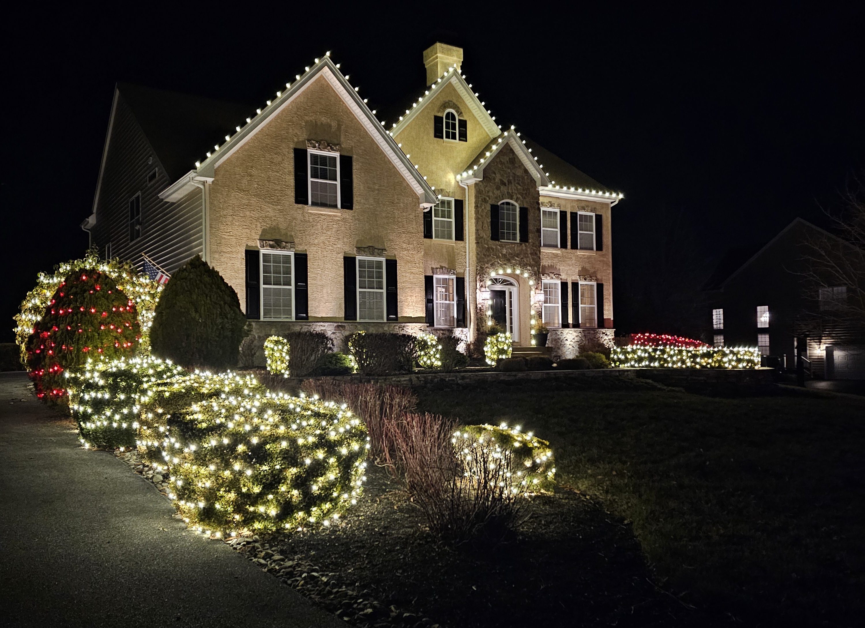 That long curve of lit hedge is what sells this one. Warm white on every gable above it, red shrubs closing off both ends.