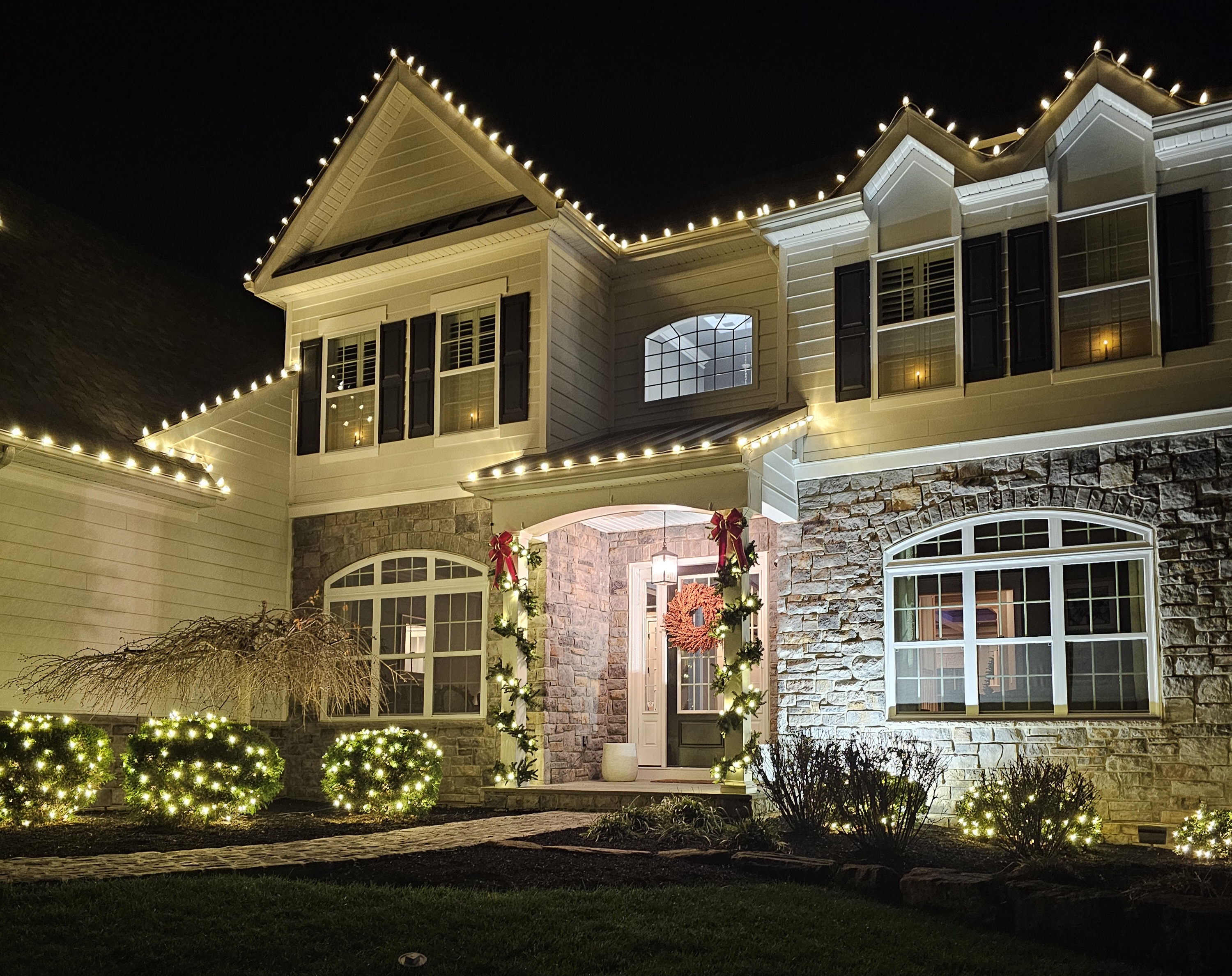 Close in on the entry — garland and red bows climbing both sides of the arch, a wreath on the door, and the beds underneath packed with light.