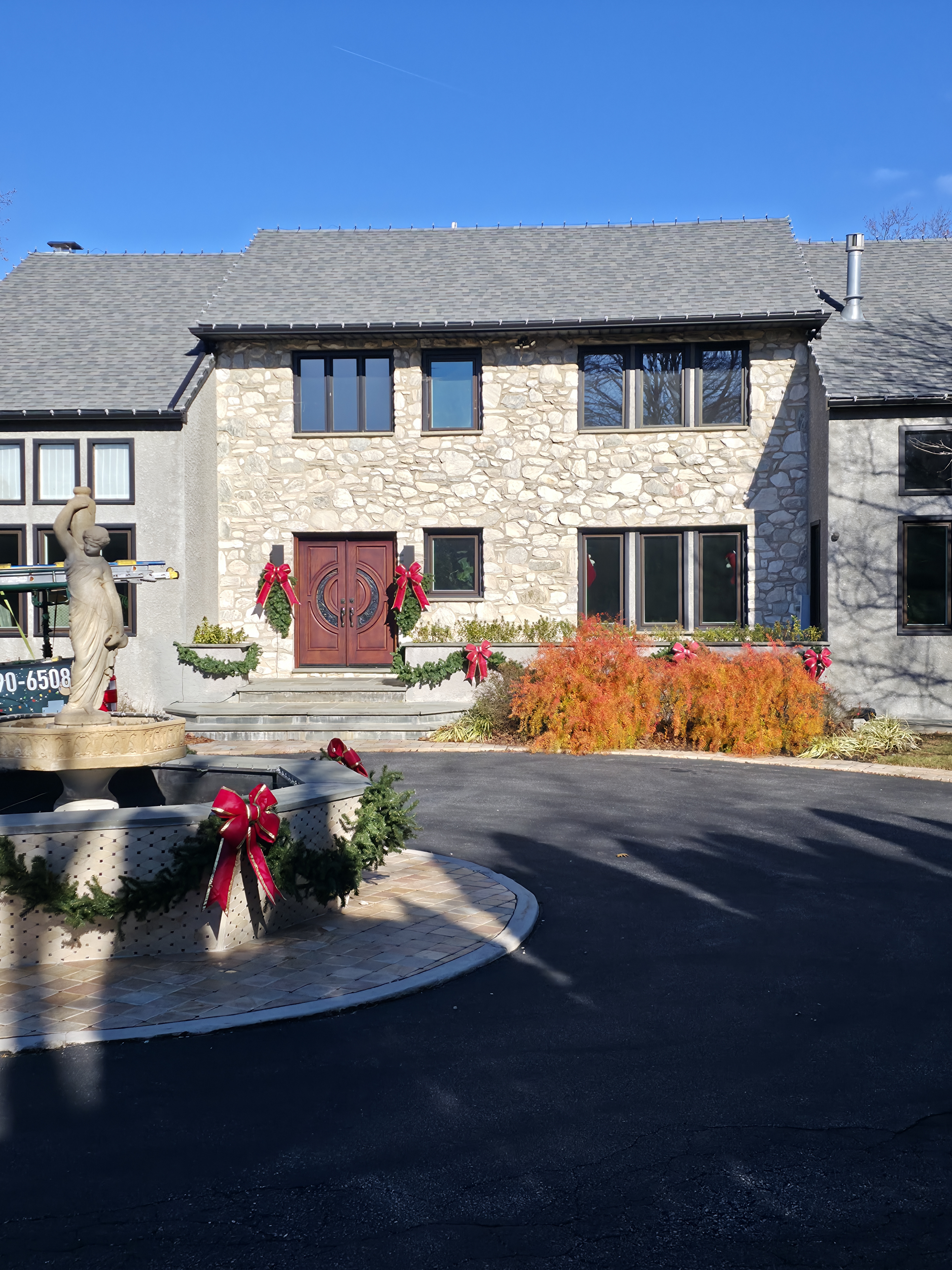 A daytime look at the greenery work: wreaths on the doors, garland and bows around the fountain and the planters, bows tied into the shrubs along the drive.